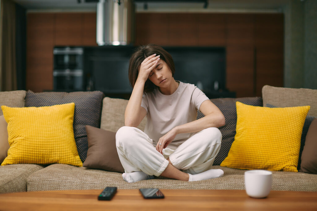 Sick young girl suffering headache or migraine, sitting on sofa at home, feel pain of sore head, morning after hangover. High quality photo